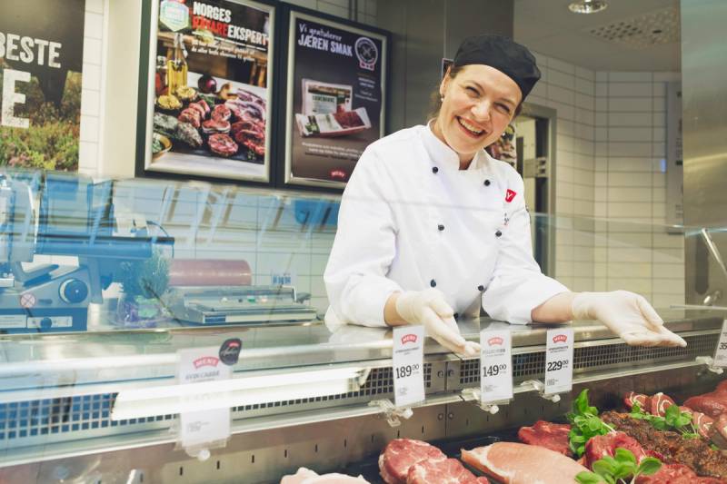 En person i hvit kokkeuniform jobber bak disken i en kjøttbutikk eller på et kjøttmarked.