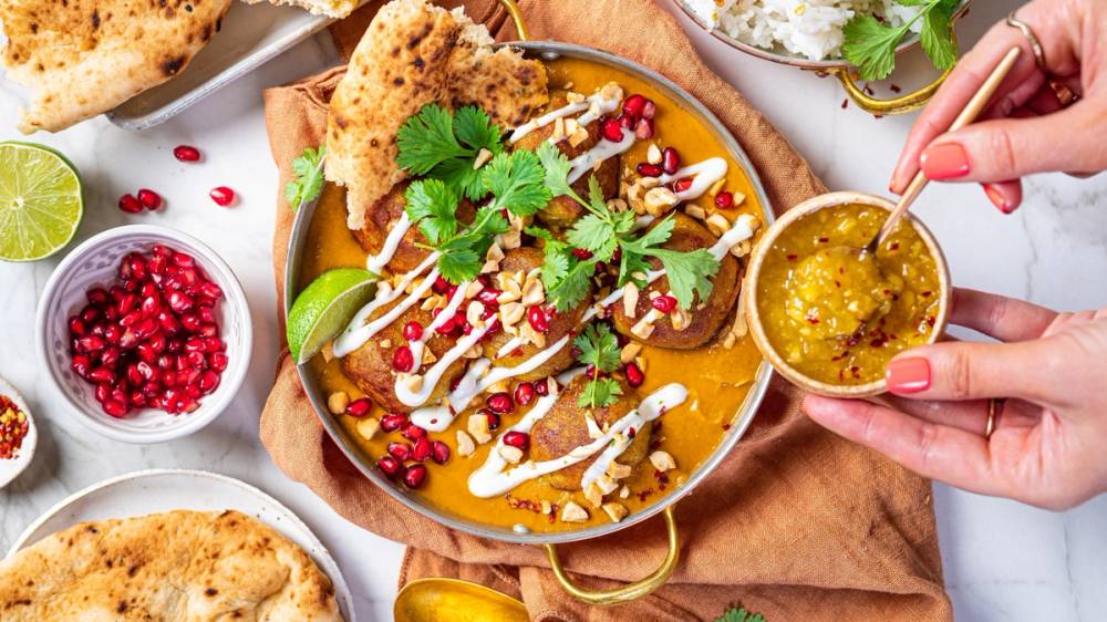 Indisk kofta med saus, pyntet med koriander og granateplekjerner, omgitt av naanbrød og limebåter.