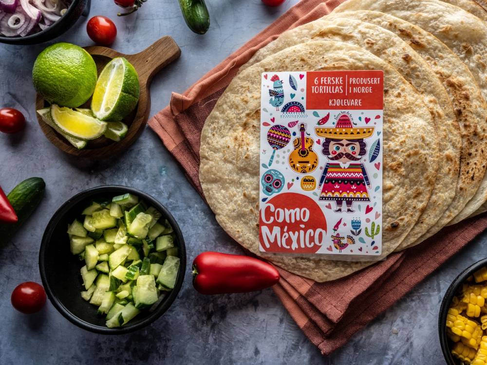 Pakke med Como Mexico produkter omgitt av lime, chili, og tortillalefser på en bordplate.