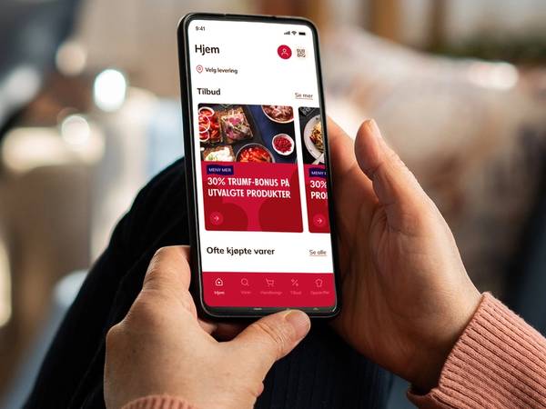 Person som holder en smarttelefon med en app som viser tilbud på matvarer fra MENY, sett fra siden.