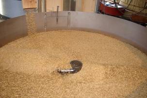 Rørbakeren fyller en stor beholder med korn eller malt, sannsynligvis for ølbrygging eller matproduksjon.