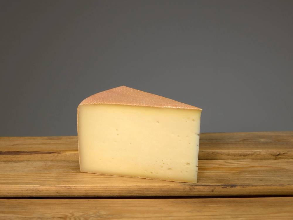 Et stykke ost på en treplate mot en grå bakgrunn.