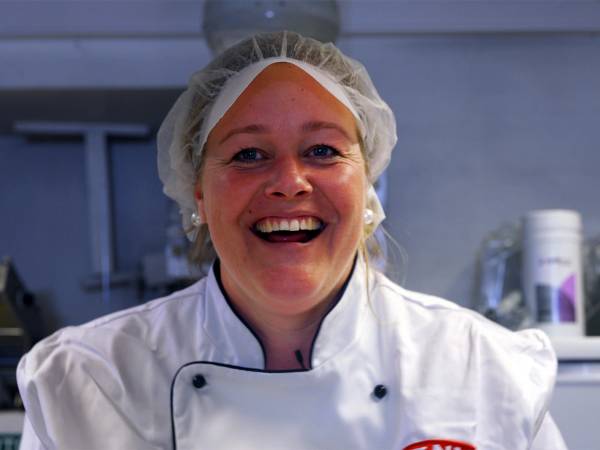 En person i kokkeforkle står foran en kjøkkenbenk med en sjokoladekake på et fat.