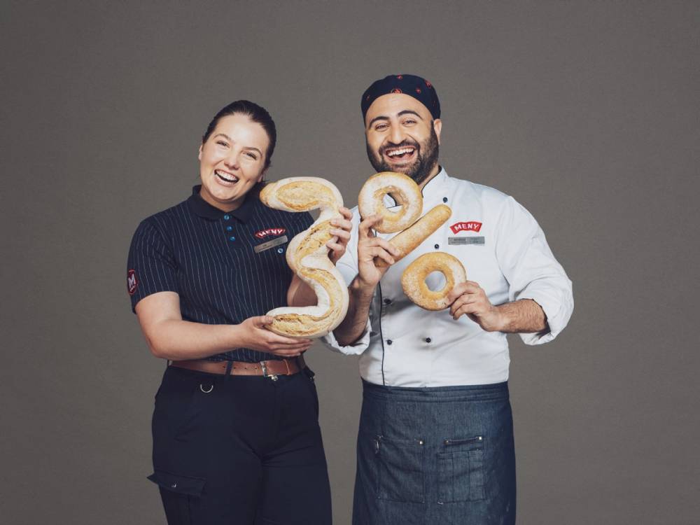 To personer holder store kaker i form av tallene 3 og 0, med teksten 'Trippel-Trumf med 3 prosent brød' i bildet.