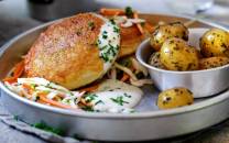 Fiskekaker med råkostsalat og små kokte poteter på en tallerken, med sitron i bakgrunnen.