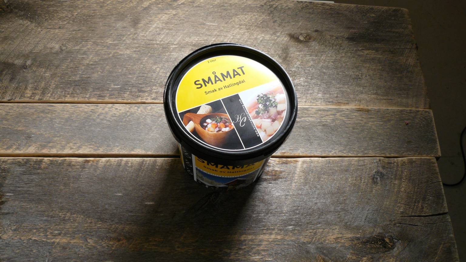 En kopp med Småmat-logo plassert på en treflate, sett ovenfra.