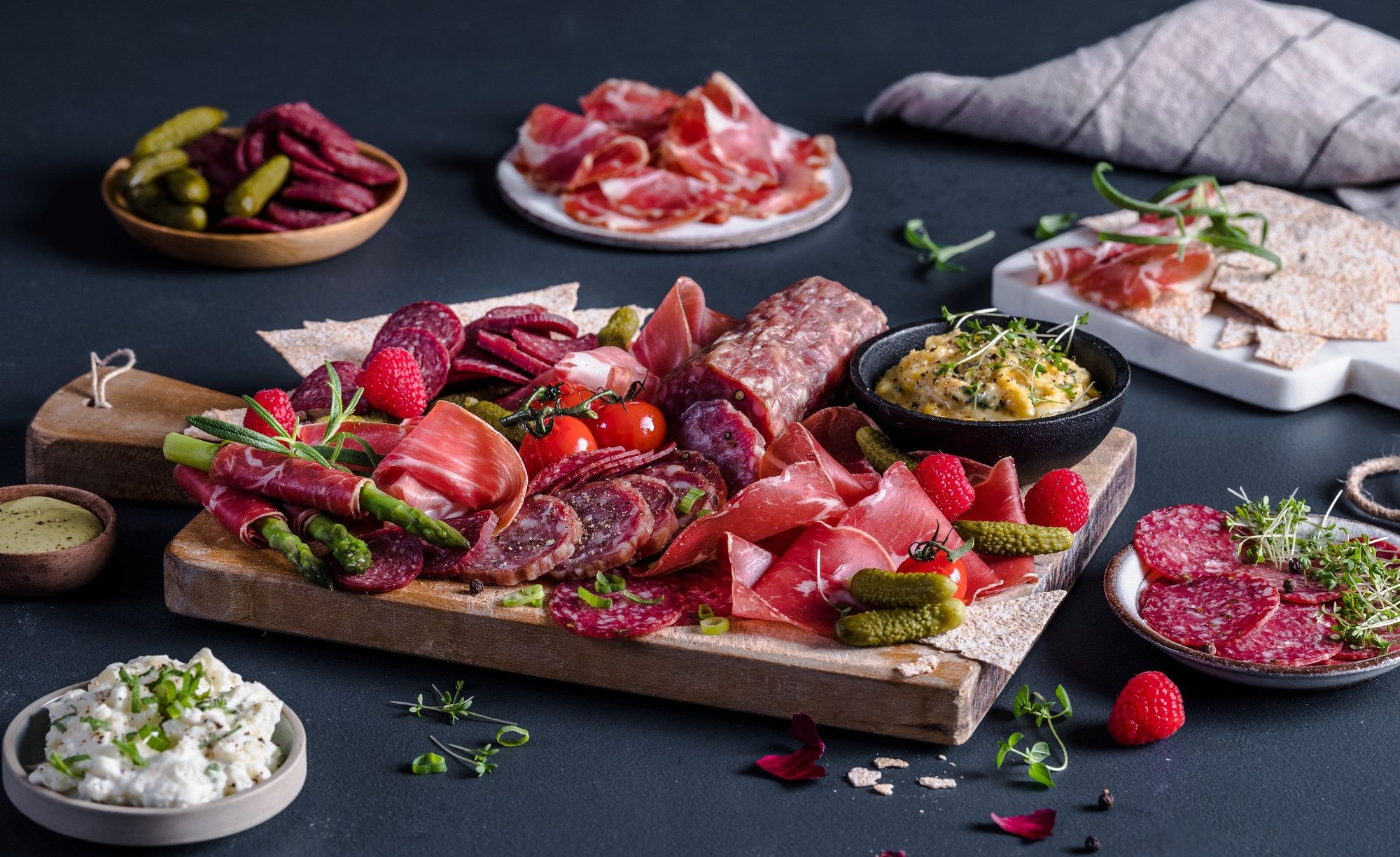 Et utvalg av spekemat, ost, grønnsaker og tilbehør på et bord, klar for helgekos.