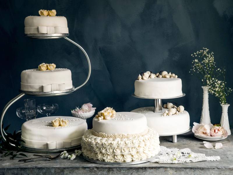 Et utvalg av bryllupskaker på et bord, med noen dekorative blomster og kaker i ulike former og størrelser.