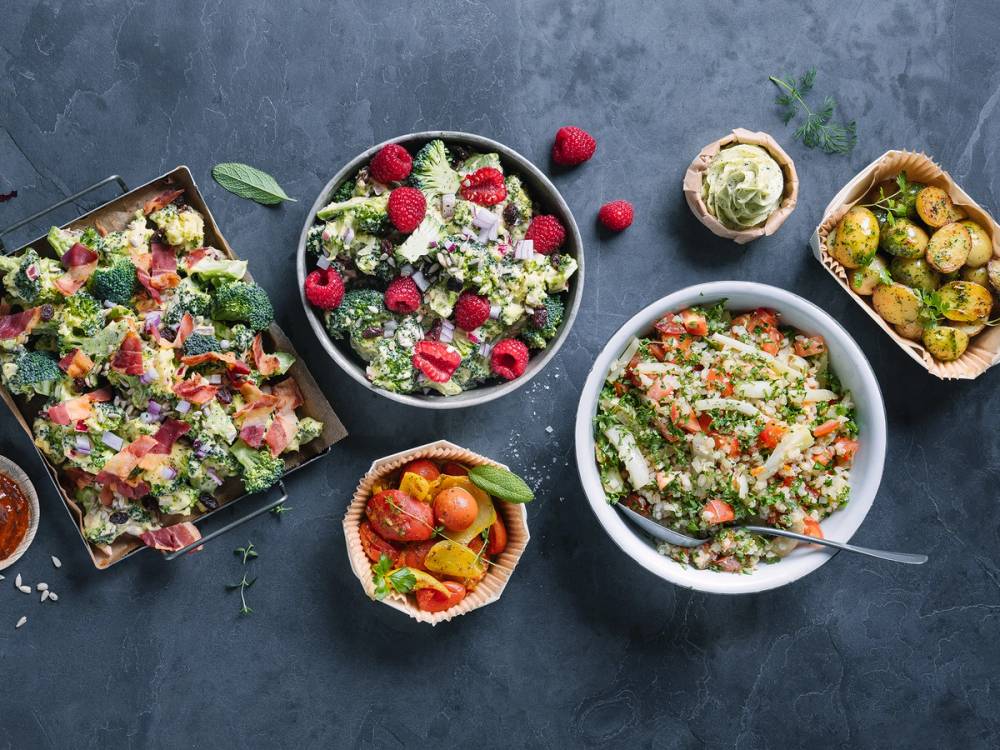 Et utvalg av sommerlige salater i ulike boller og fat på en mørk bakgrunn.