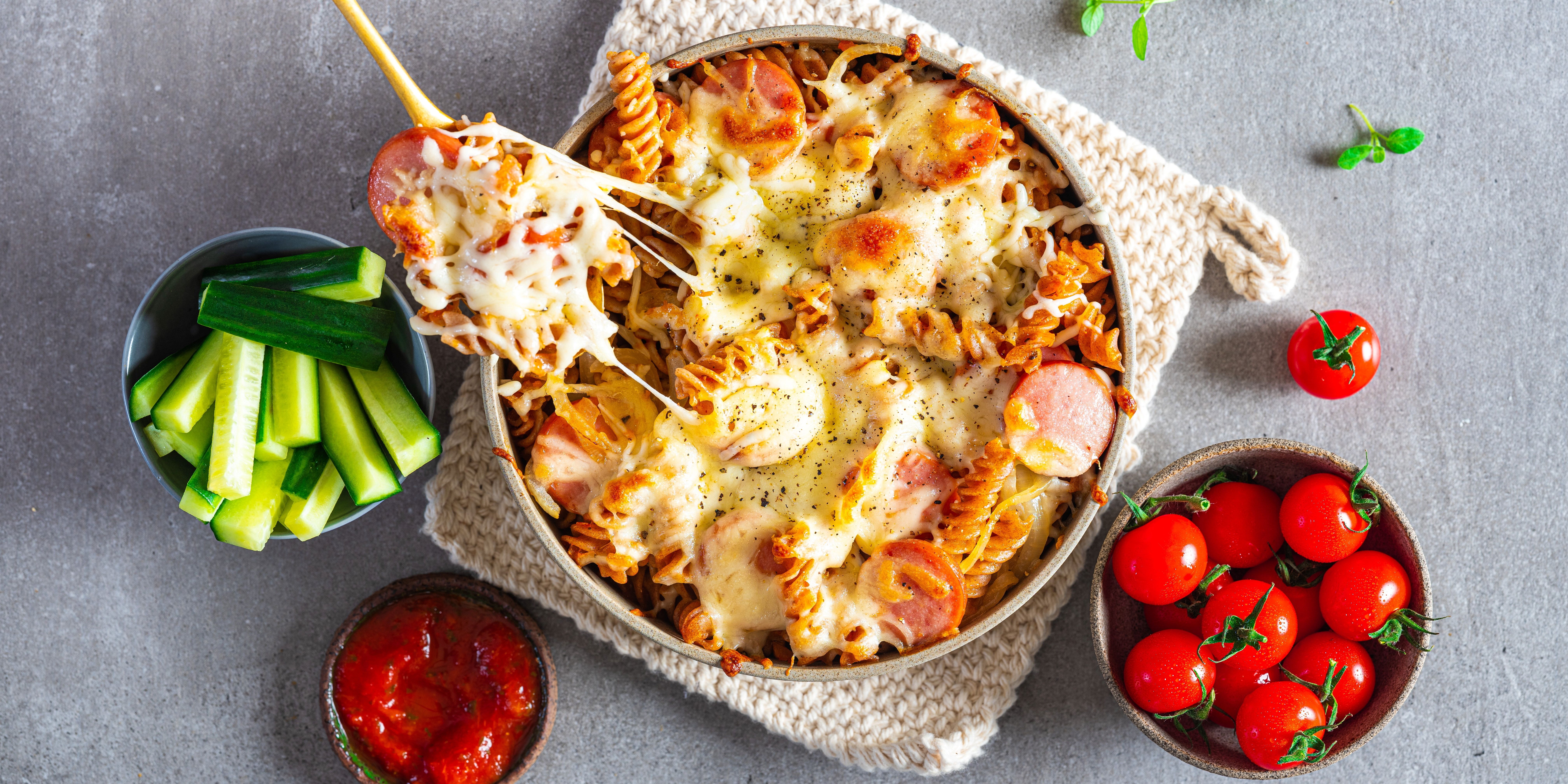 En pizza med skinke og ost, omgitt av cherrytomater og selleristenger, på et bord.