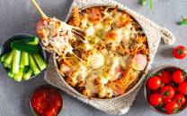 En pizza med skinke og ost, omgitt av cherrytomater og selleristenger, på et bord.