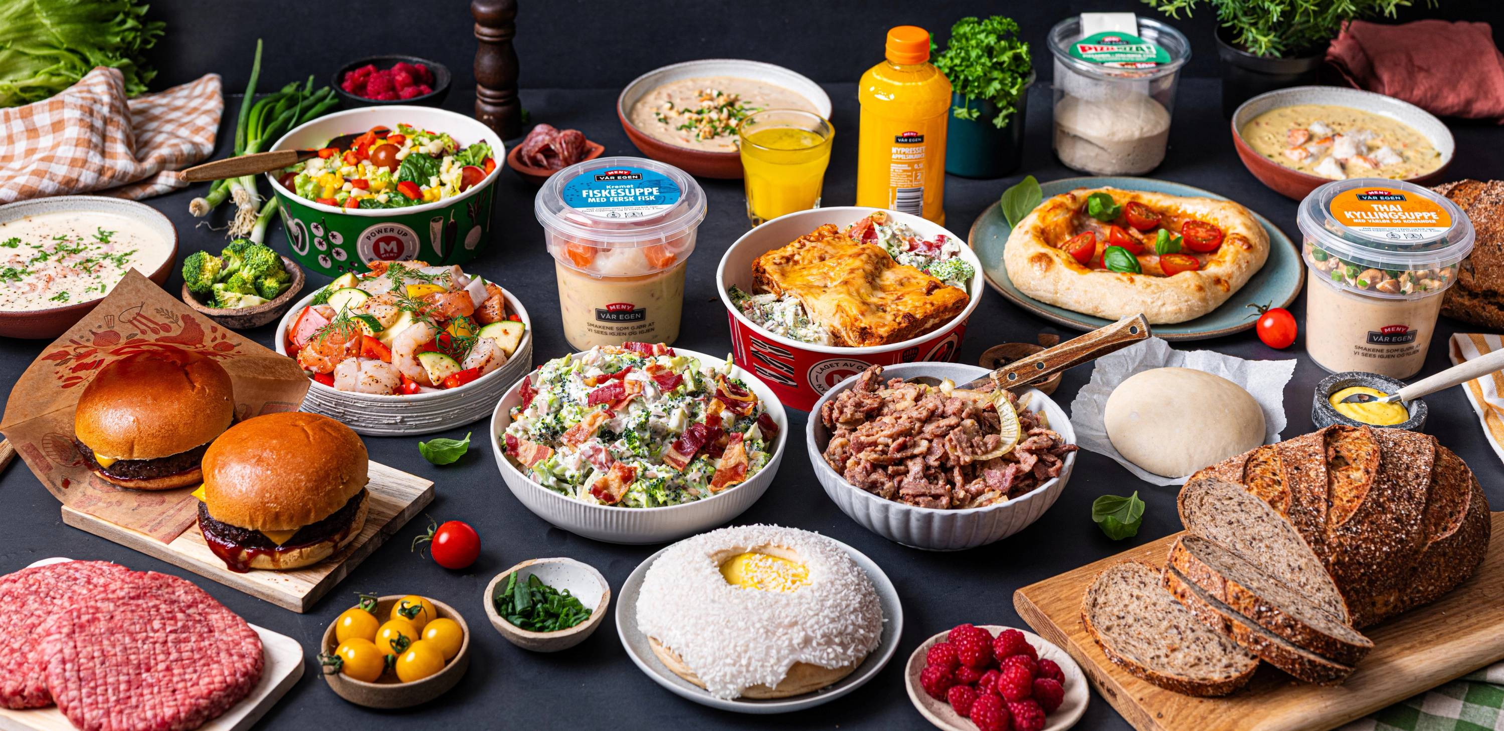 Et utvalg av ulike middagsretter og tilbehør på et bord, inkludert burgere, salater, brød og desserter.