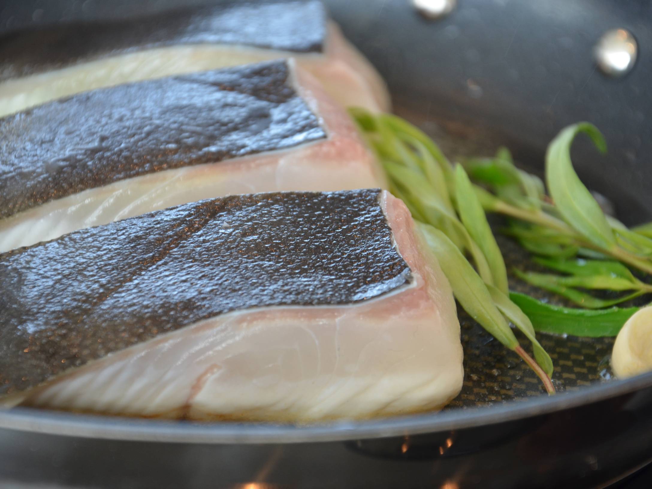 Sterling kveitefilet stekes i panne med grønne urter ved siden av.