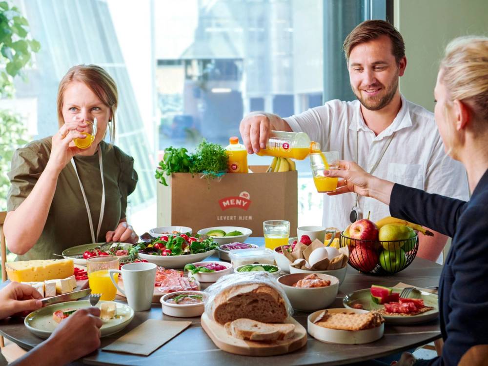Tre venner som sitter rundt et bord og koser seg med en god frokost.