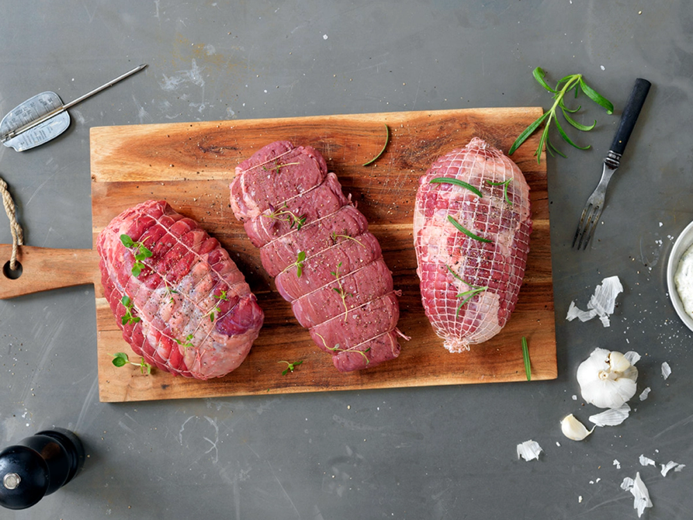 Tre rå biffer ligger på et skjærebrett med krydder og urter rundt, klare for steking.