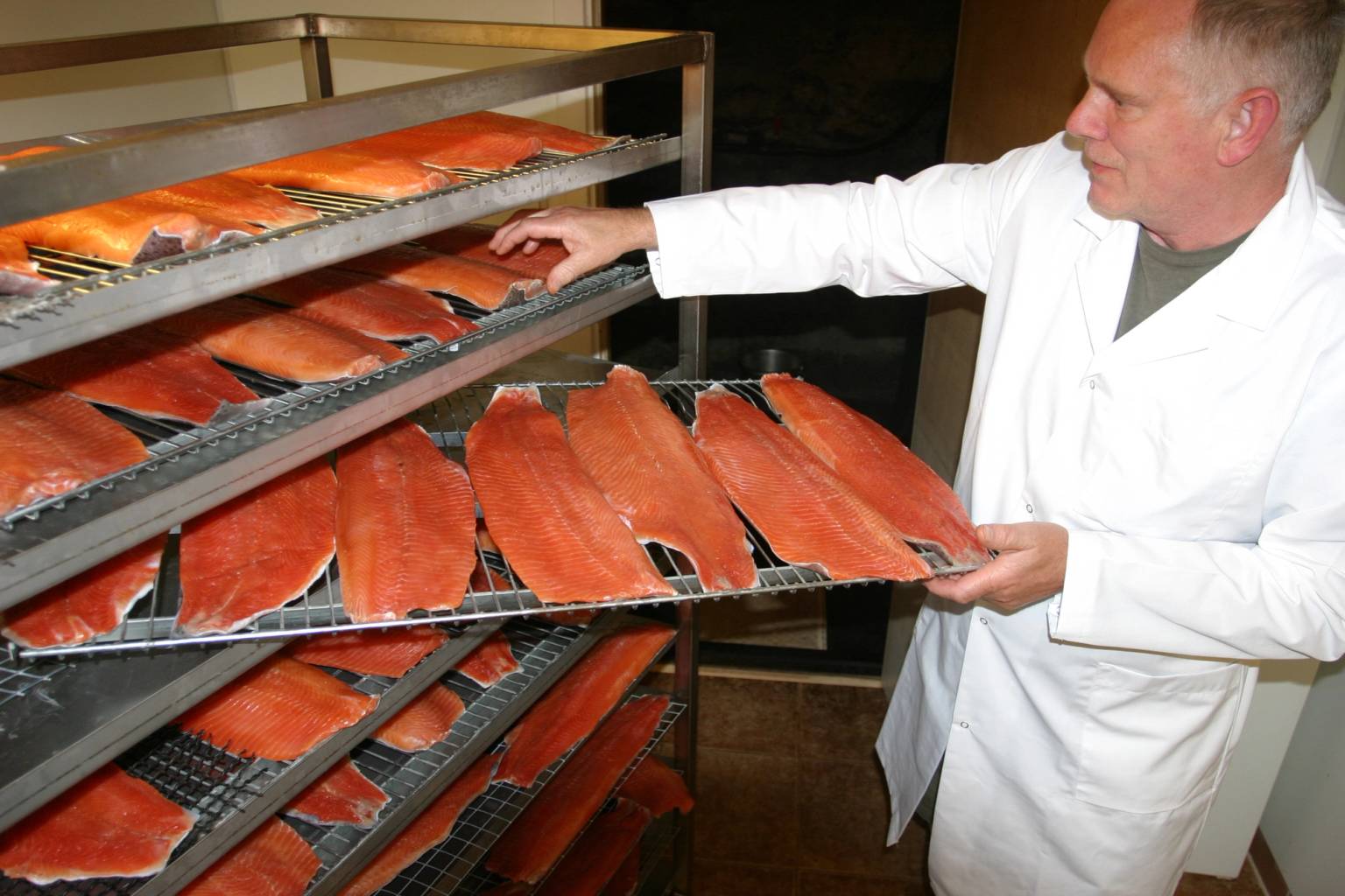 Person som håndterer laksefileter på en produksjons- eller lagringshylle, med flere laksefileter på rad.