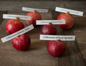Fem røde epler med navnelapper på en treplate, der det står 'Velkommen til bords' og navnene på personer.