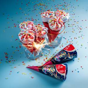 To glass med iskrem toppet med fargerikt strøssel, omgitt av konfetti og festpynt på en blå bakgrunn.