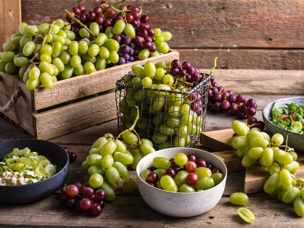 Bilde av grønne og røde druer i kurver og skåler på et trebord.