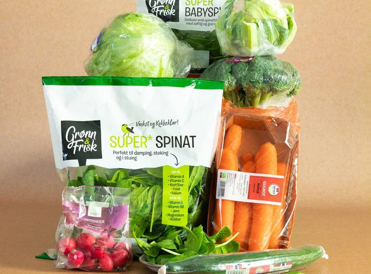 Frukt og grønnsaker i plastposer, inkludert salat, gulrøtter, reddiker og agurk, på et bord.