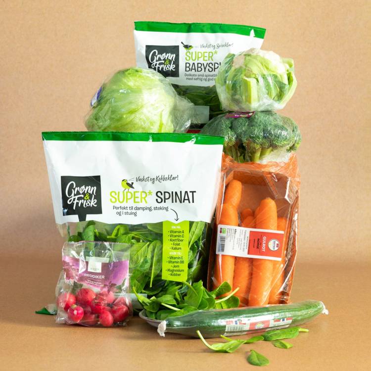 Frukt og grønnsaker i plastposer, inkludert salat, gulrøtter, reddiker og agurk, på et bord.