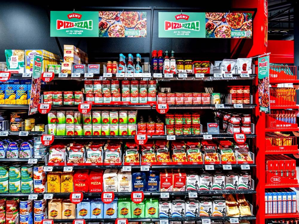 Hylla i en dagligvarebutikk med ulike typer pizzasaus og ferdigmatprodukter, med en Pizza Pizza-banner øverst.