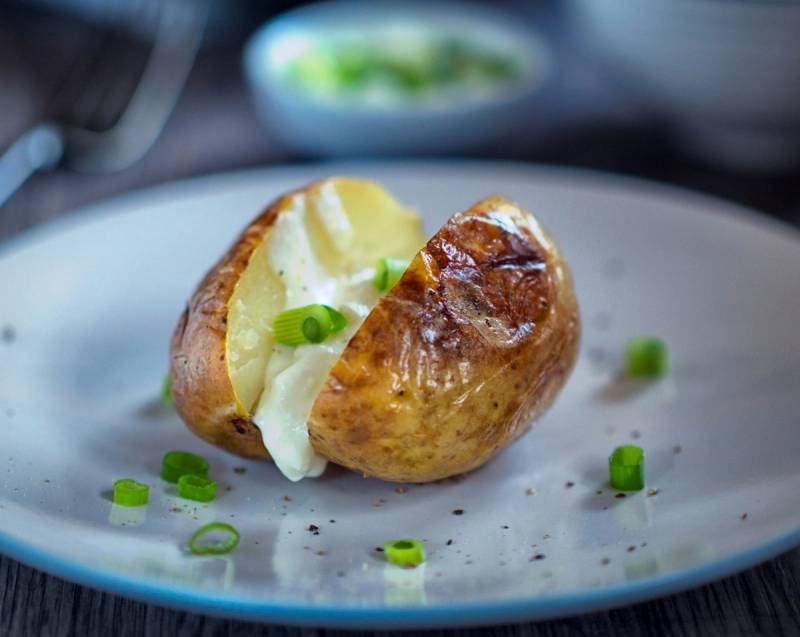 Bakt potet fylt med smør og hakket grønn løk på en tallerken