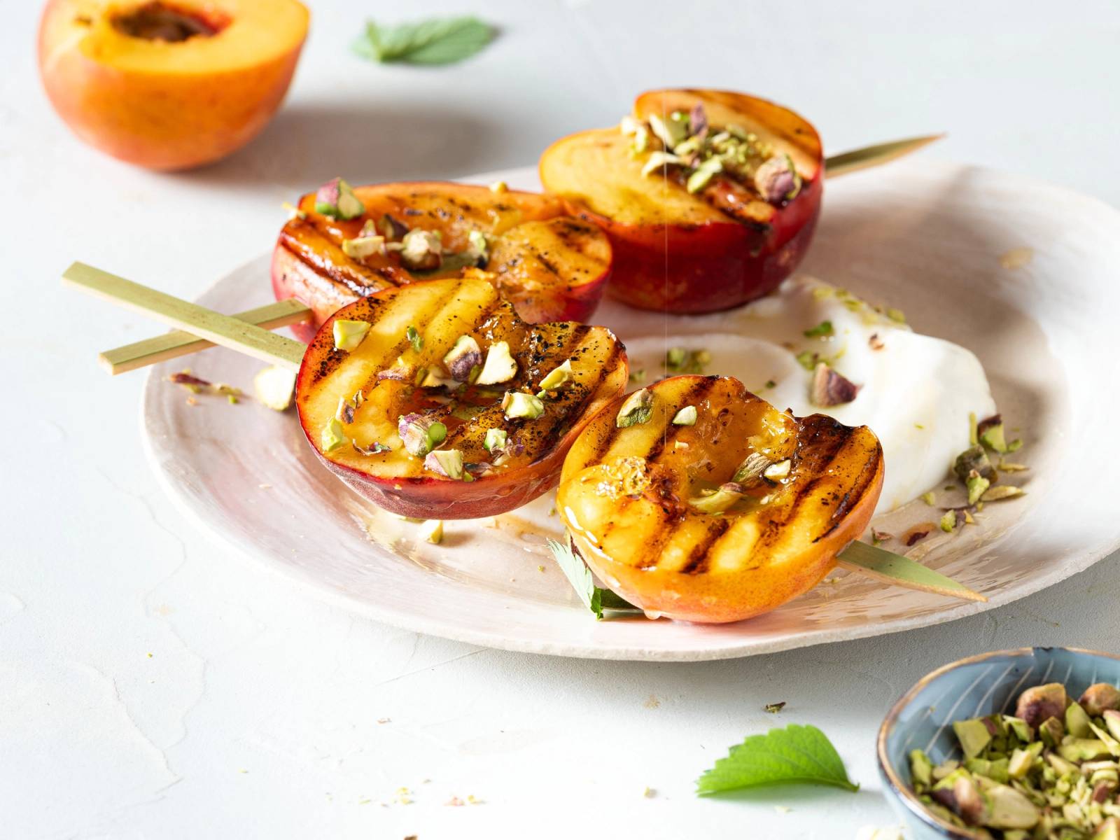 Fersken fylt med nøtter og honning, ser ut til å være grillet eller bakt, servert på en hvit tallerken med en skje ved siden av.