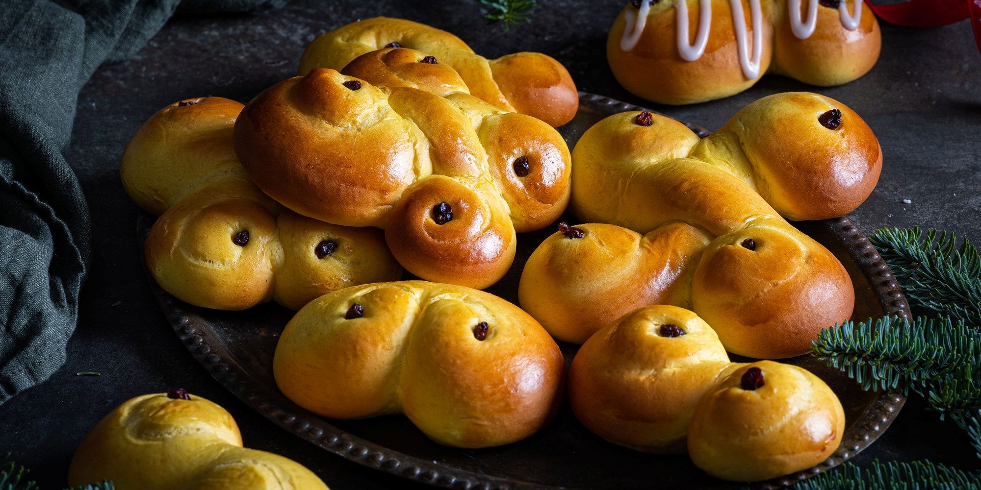 Lussekatteformede boller med rosiner, pyntet med melisglasur på toppen, på et fat.