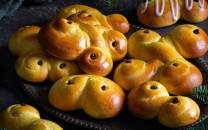 Lussekatteformede boller med rosiner, pyntet med melisglasur på toppen, på et fat.