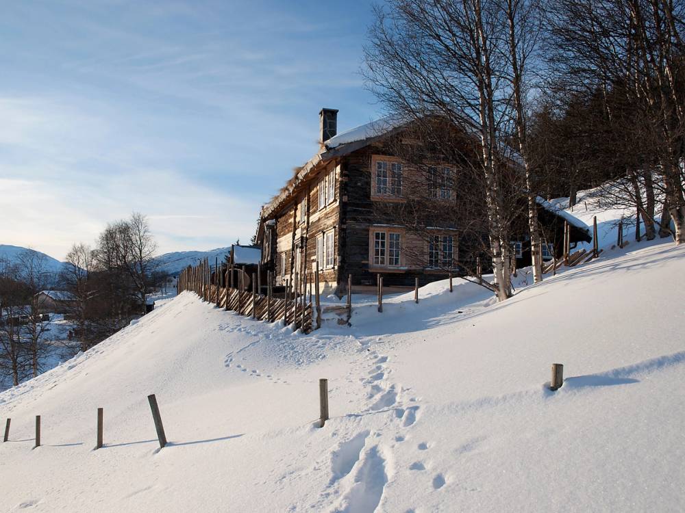 En stor trebygning på en snødekt ås med trær rundt og fjell i bakgrunnen, tatt i Hovden i Agder.