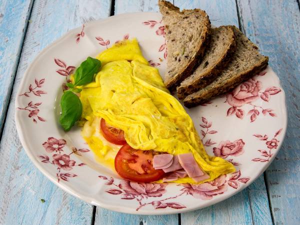 Omelett med tomat, skinke og basilikum servert med brødskiver på en blomstrete tallerken.