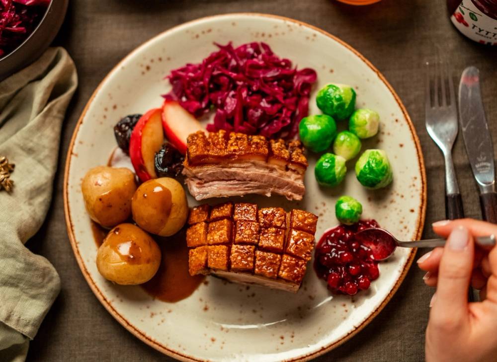 En tallerken med svinekjøtt, poteter, rødkål, tyttebær og grønne erter, med bestikk ved siden av.