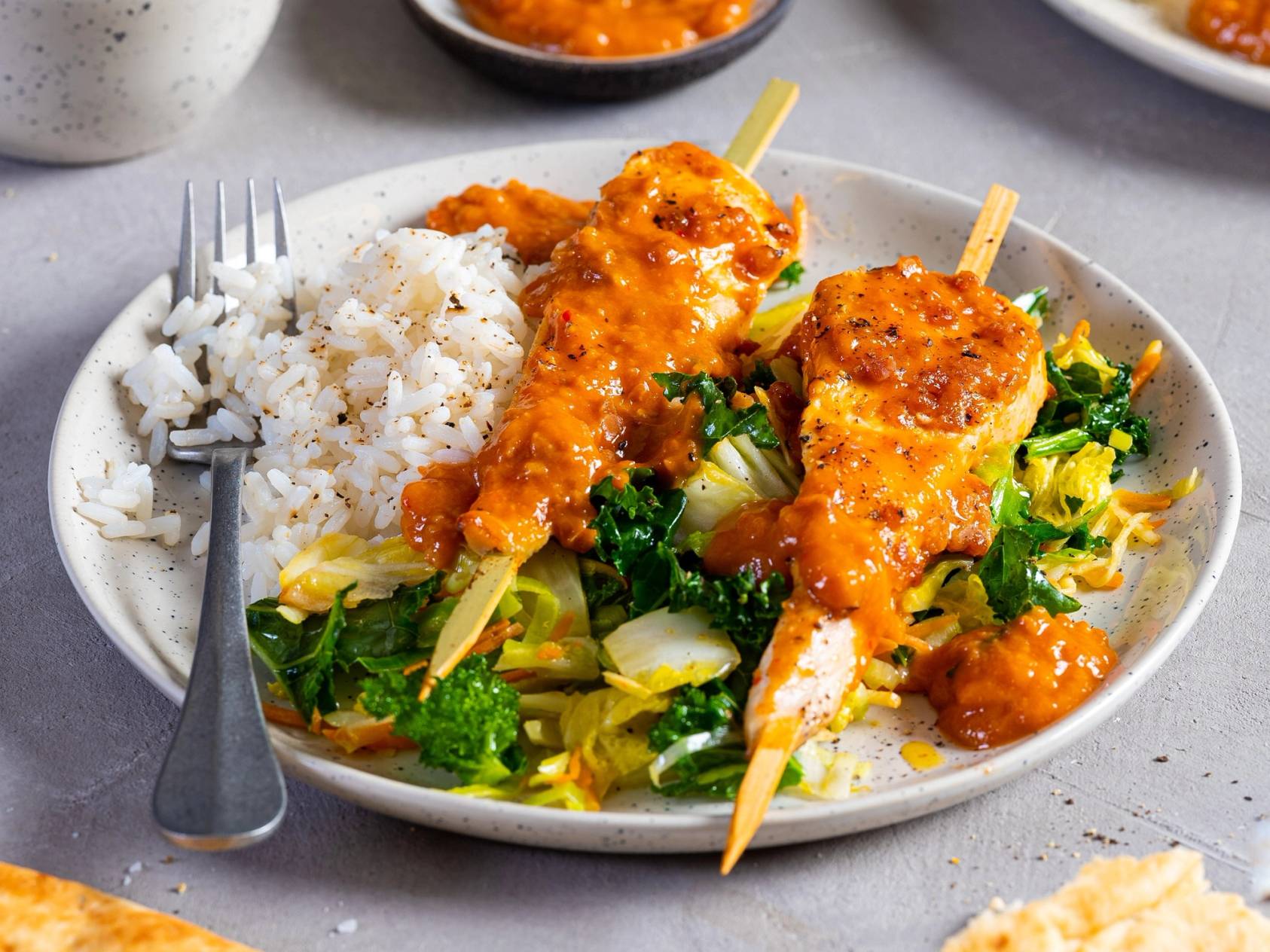 Kylling satay servert med ris og grønnsaker på en hvit tallerken