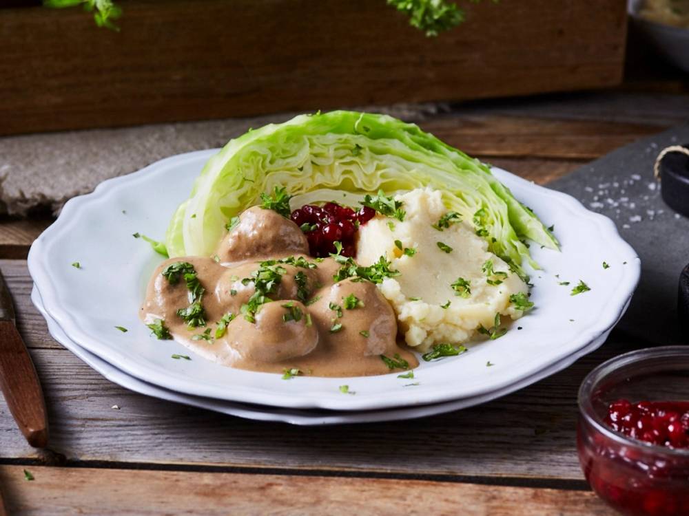 Kjøttboller i fløtesaus med potetmos og kål på en hvit tallerken