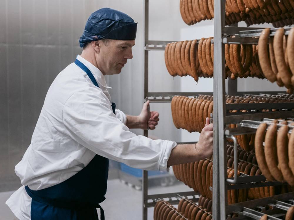 Person som jobber med å henge opp rå pølser på en metallrist i en produksjonsfasilitet.