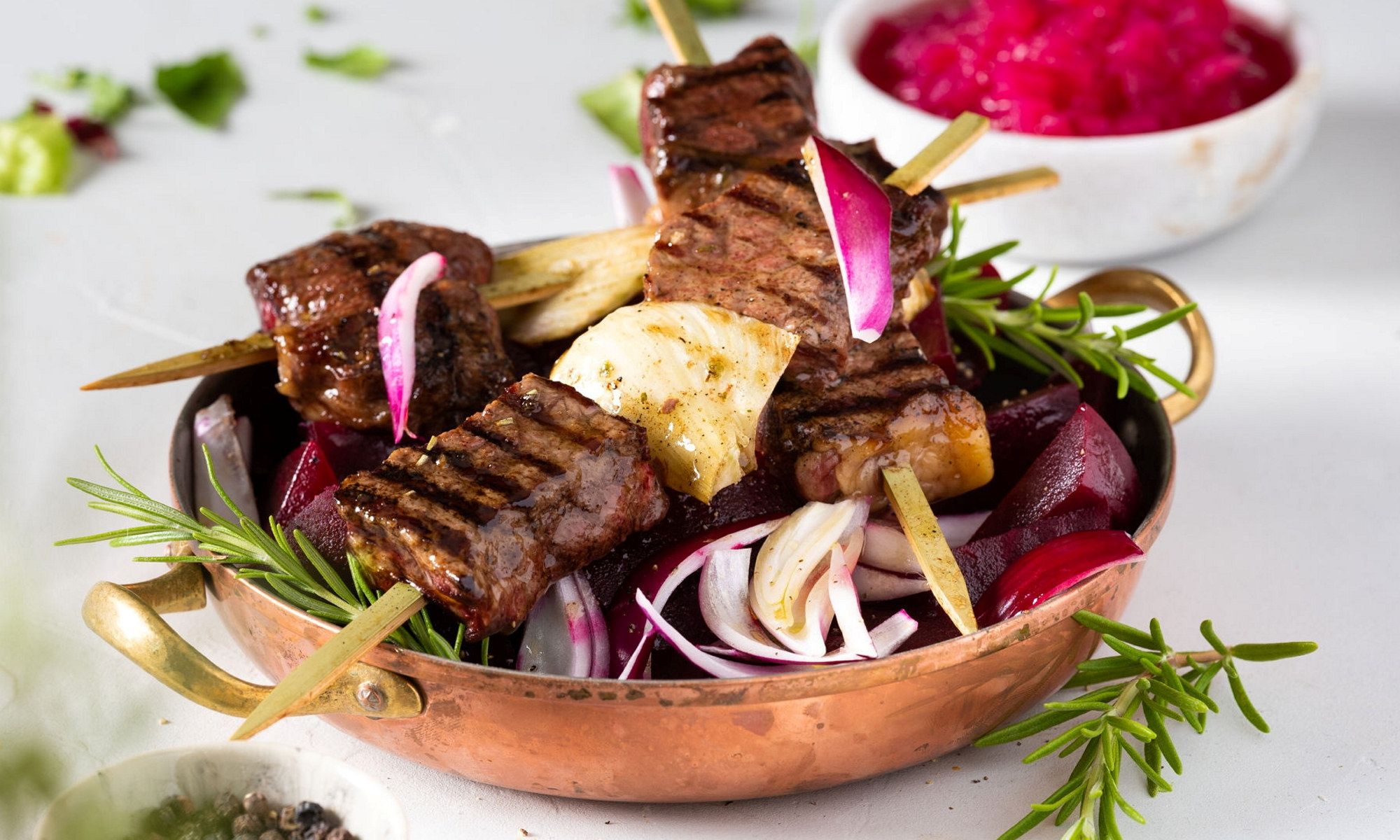 Grillspyd med marinert biff og fennikel på en tallerken med grønnsaker og urter.