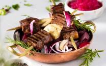 Grillspyd med marinert biff og fennikel på en tallerken med grønnsaker og urter.