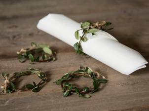 En hvit serviett er brettet og pyntet med små grønne blader, lagt på en treoverflate.