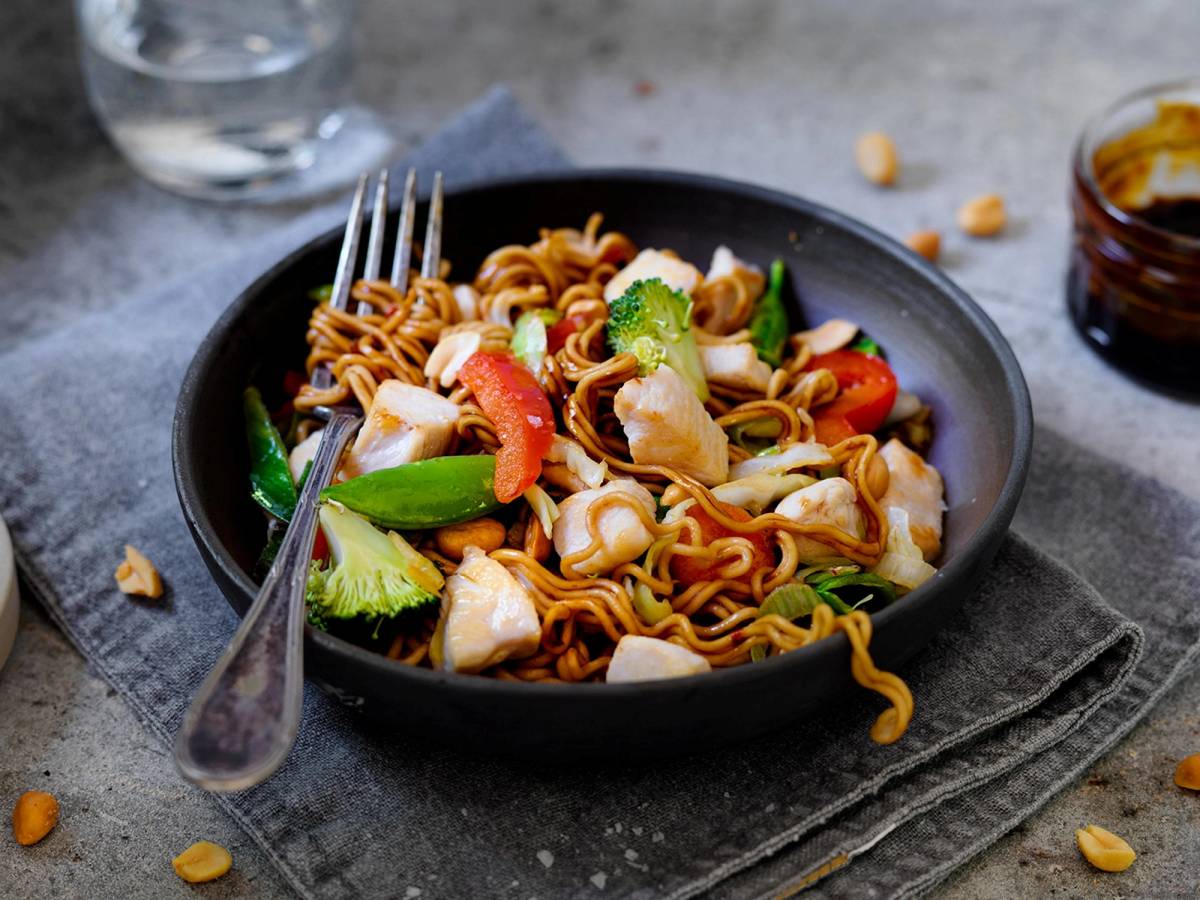 Spicy kyllingwok med grønnsaker i en svart skål på et bord.