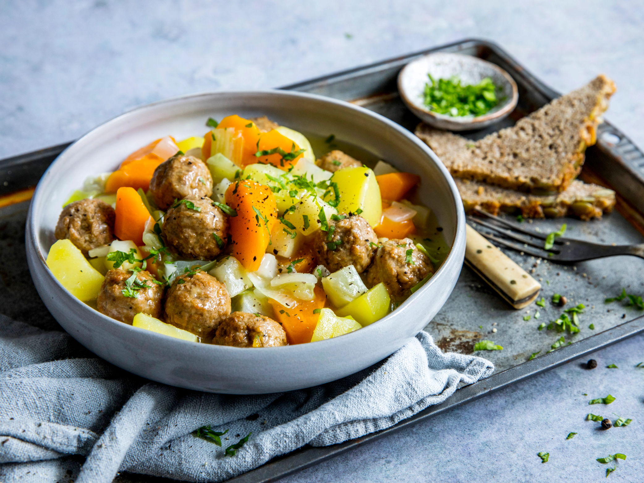 Kjøttfri lapskaus med grønnsaker og kjøttboller i en hvit bolle, servert med brød og urter på siden.