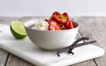 En hvit bolle med jordbær og mascarponeost, med en limebåt og vaniljestang ved siden av på et skjærebrett.