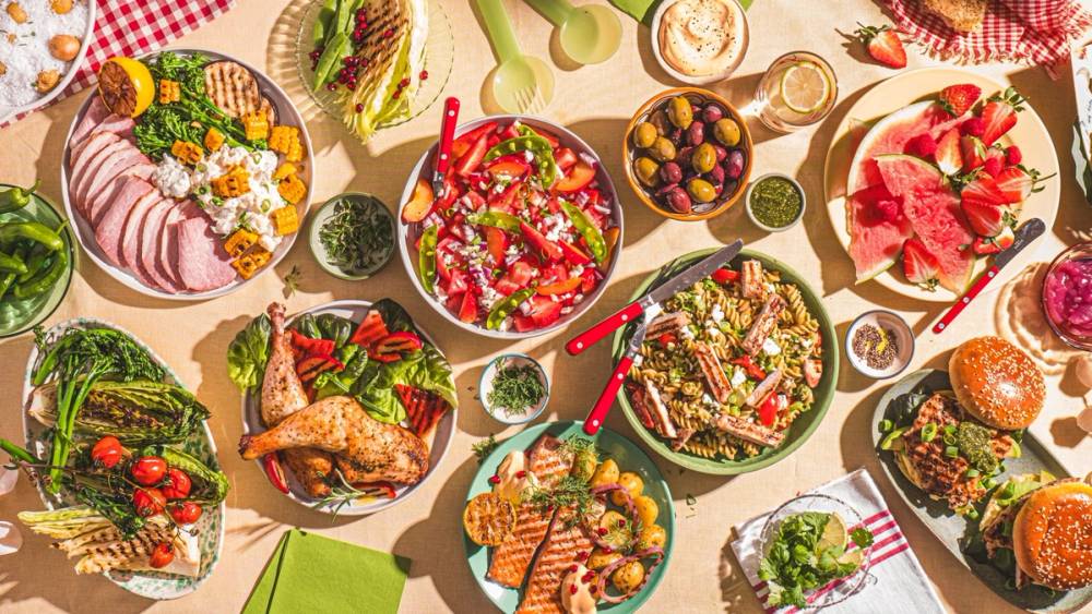 Et bord dekket med ulike sommerretter, salater, frukt og grønnsaker på en festlig måte.