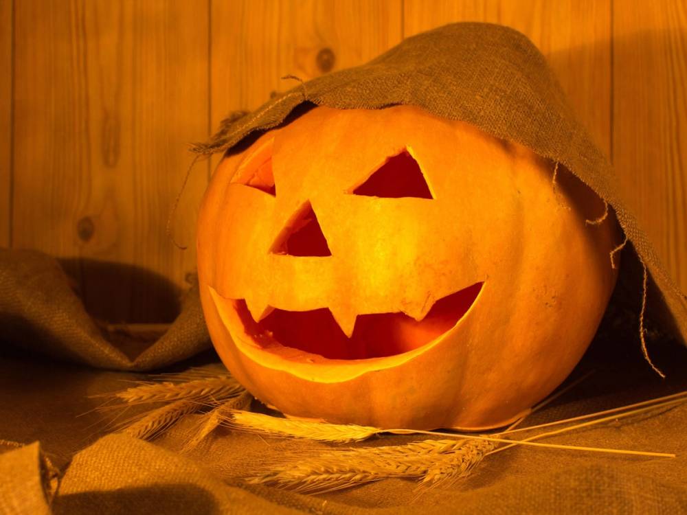 En uthultet gresskar med ansikt, brukt som Halloween-dekorasjon, plassert på et bord med en trevegg i bakgrunnen.