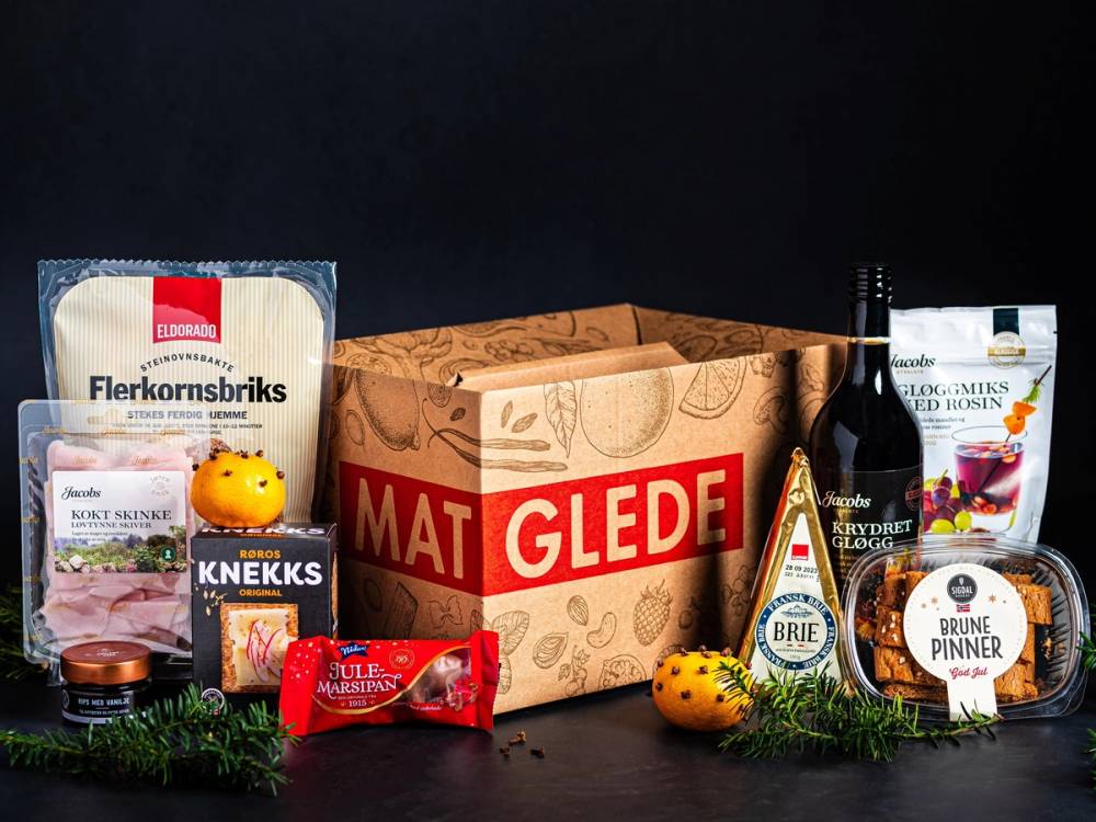 Gaveesker med mat- og drikkevarer, inkludert en pakke med kjøtt, en flaske vin, og ulike små matvarer, på en mørk bakgrunn.