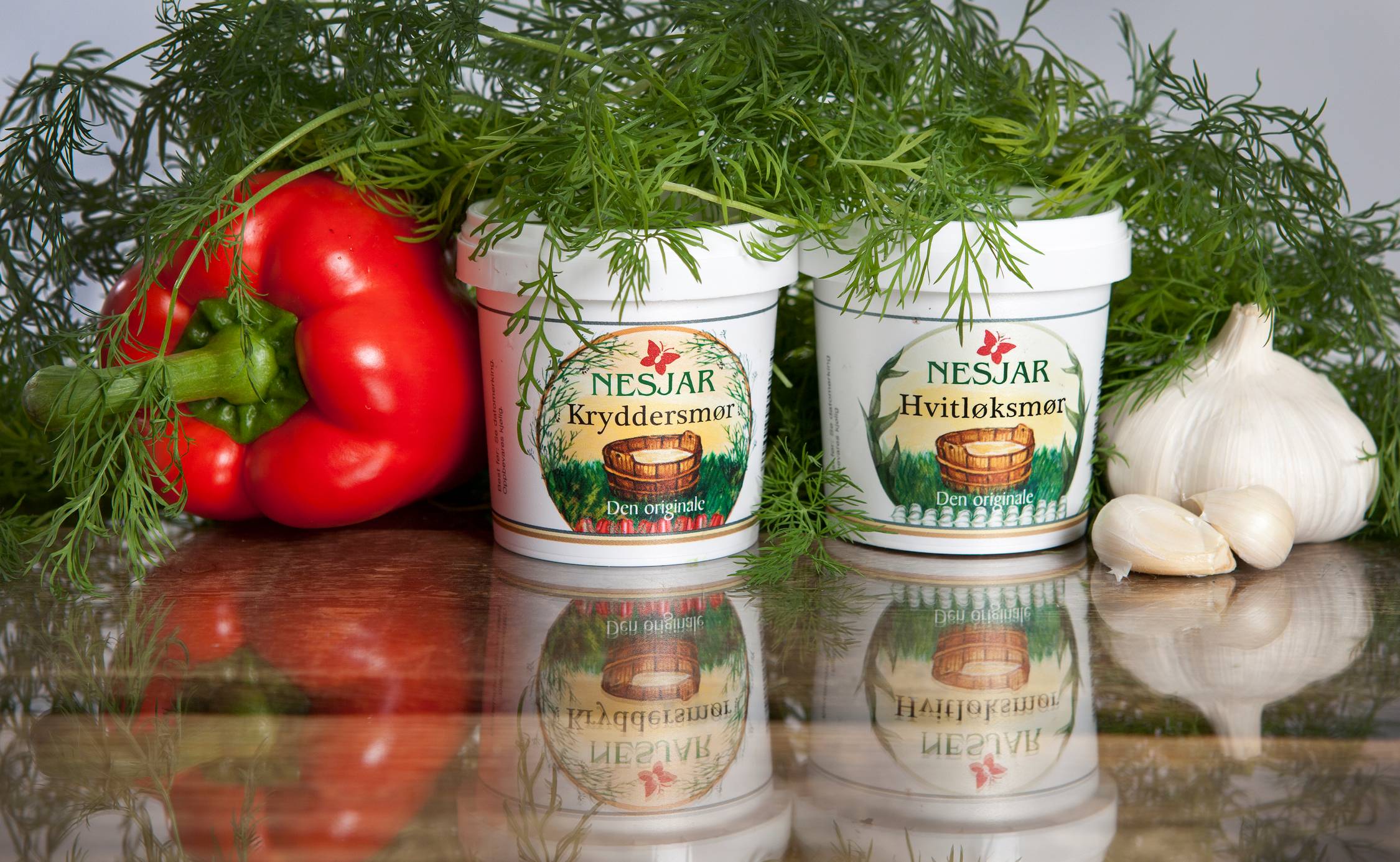 Nesjar krydderurter i hvit plastbeholdere, omgitt av en rød paprika og hvitløk, med ferske grønne urter i bakgrunnen.