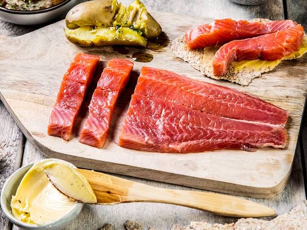 Ulike typer av rakfisk på et skjærebrett med tilbehør som smør, syltetøy og grønnsaker, klar til servering.