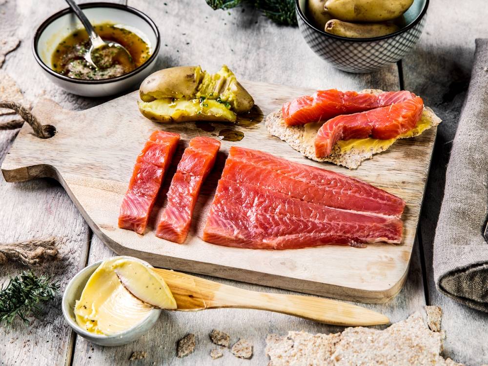 Ulike typer av rakfisk på et skjærebrett med tilbehør som smør, syltetøy og grønnsaker, klar til servering.