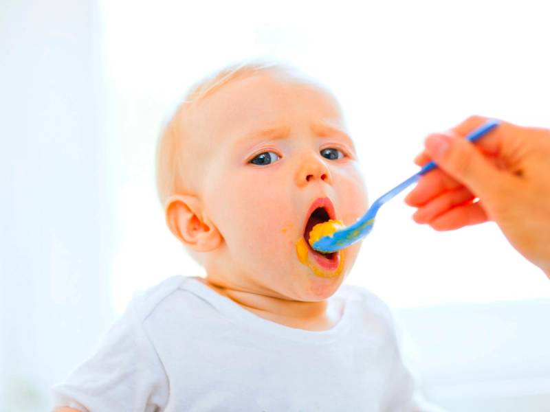 Et barn blir undersøkt med en skje i munnen av en person med hansker, uten å vise ansiktet til barnet.