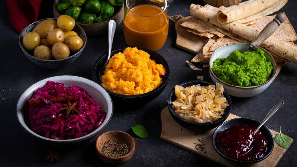 Et utvalg av julemat og tilbehør, inkludert poteter, gulrotmos, rødkål, grønnsaker, saus og brød, på et bord.